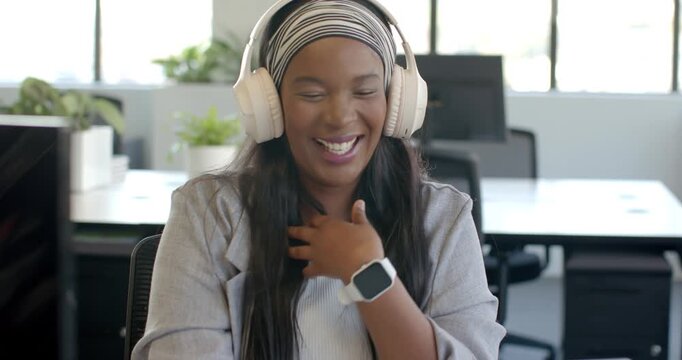 African woman hearing ping via headphones, laughing, leaning toward laptop to read message