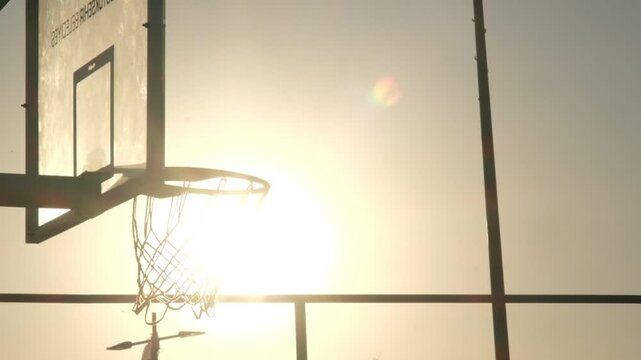 A dramatic slow motion close up video of a basketball ball going through a silhouette hoop and net, capturing precise athletic movement and dynamic sports action in detail.