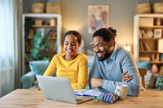 Father and daughter doing homework with laptop at home. Father and teenage girl happy using laptop. Teen girl and dad sitting at home working with notebook