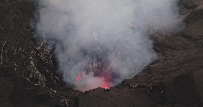 Volcano crater actively erupting with glowing molten lava, hot ash, and plumes of smoke rising from the raw, dark landscape of Mount Yasur Tanna Island, Vanuatu. Dramatic night scene. Aerial panorama