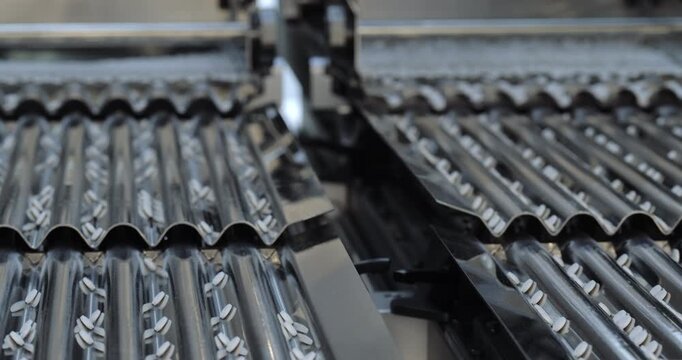 Automated sorting machine guides tablets through corrugated metal channels. Precision equipment separates medicine units into orderly lanes for processing