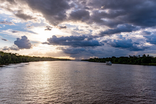 Dramatic sunset sky with sun rays and storm clouds over the Amazon River with distant regional boat