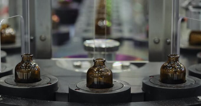 Rotary conveyor moves amber glass bottles toward automated capping machine. Indexed holders position each container for controlled closure processing in factory