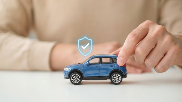 A person protecting a blue toy car with a digital shield symbol. Car insurance concept for safe driving and vehicle protection.
