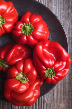 Top view of red bell peppers in dark plate. Rustic kitchen styling, fresh organic harvest