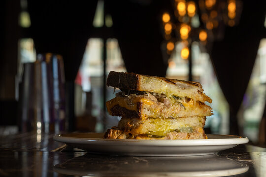 Gourmet toasted sandwich with melted cheese and pulled meat on plate in cozy restaurant