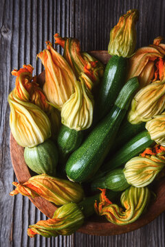 Assorted zucchini with blossoms in wooden bowl, fresh organic vegetables, farm harvest concept. Green squash and edible flowers top view, natural texture, healthy ingredient