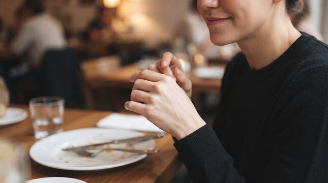 A young woman enjoys a meal at a restaurant, the focus on her hands as she prepares to eat, hinting at anticipation and a moment of quiet enjoyment.