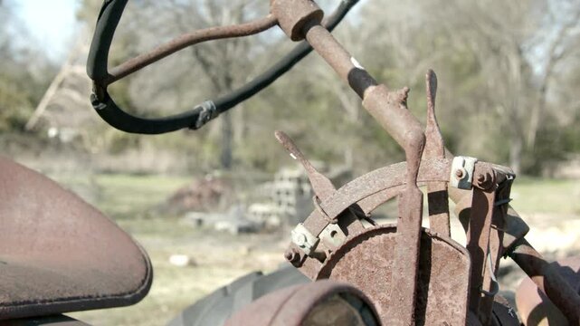 Slow panning detail shot of an old farm tractor rusting in the sun.