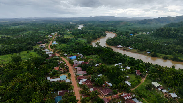 Aerial view of a tropical riverside village surrounded by lush forest and hills