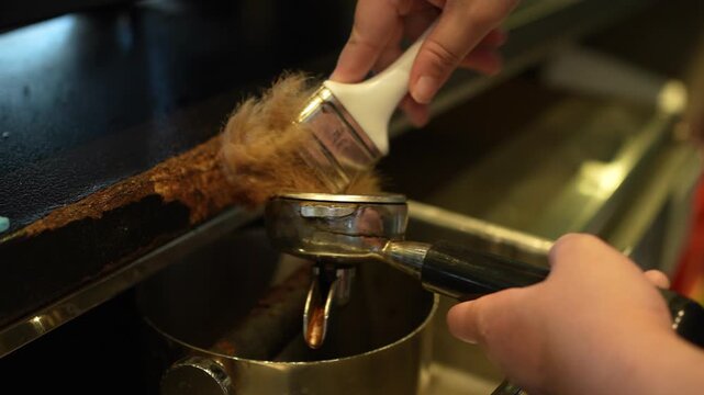Barista cleaning used coffee grounds from an espresso portafilter with a brush