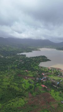 Vertical drone view of serene Pawna Lake with rolling green hills and foggy monsoon clouds in Maharashtra⁠