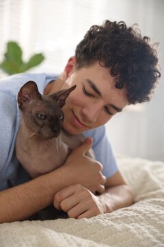 Teenage boy with Sphynx cat on bed at home. Adorable pet