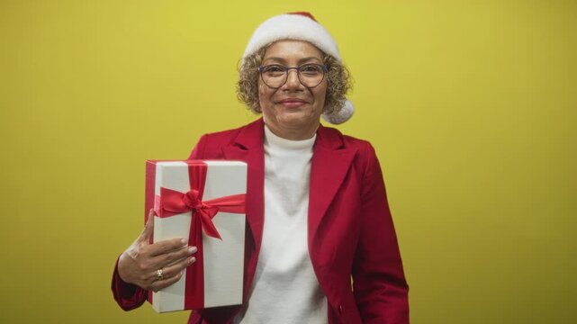 Woman holding gift with hand visible, wearing santa hat and red jacket in studio; festive giving warmth.