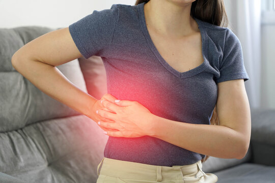 Intercostal pain concept. Unrecognizable young woman with hands on her ribs. Painful area is highlighted in red.