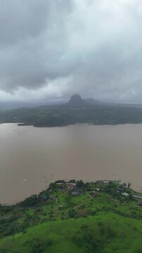 Vertical drone view of serene Pawna Lake with rolling green hills and foggy monsoon clouds in Maharashtra⁠