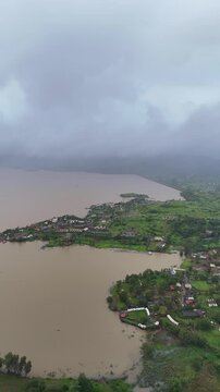 Vertical drone view of serene Pawna Lake with rolling green hills and foggy monsoon clouds in Maharashtra⁠