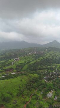 Vertical drone view of serene Pawna Lake with rolling green hills and foggy monsoon clouds in Maharashtra⁠