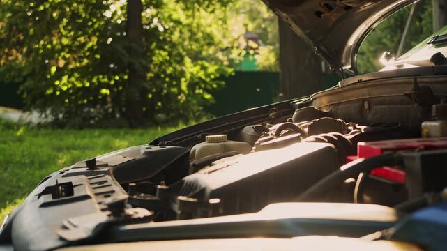 Driver opens the hood and examines the engine bay during a car breakdown on a sunny summer day.