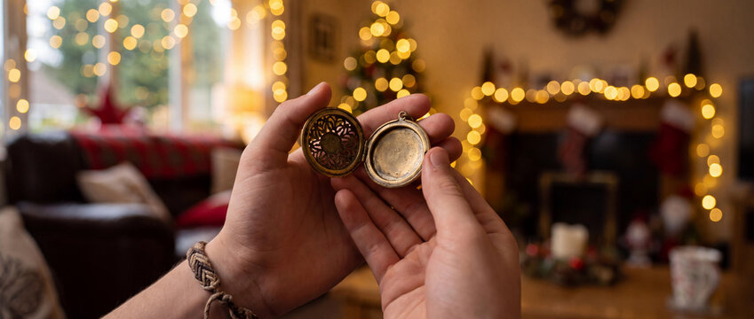 Hands holding an open vintage bronze locket in a cozy Christmas living room with bokeh lights