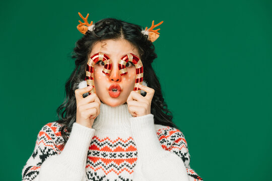 Playful woman with candy canes and reindeer antlers on green background