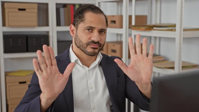 Man hands raised palms out inside building office storage wearing suit and white shirt with shelves and desk visible; refusal boundary.