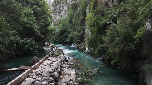 Cinematic view of a wild turquoise river flowing through a lush green rocky canyon.