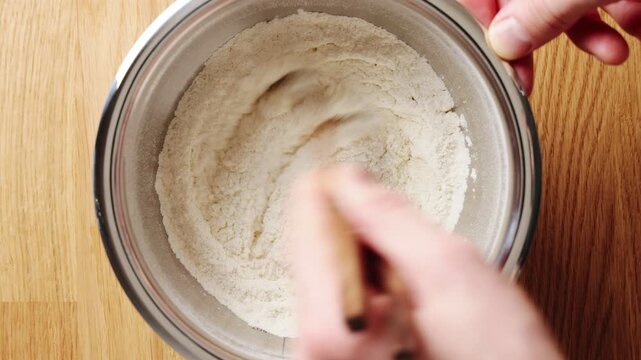 Chopsticks stir dry flour in bowl and add air. Mixing flour breaks small lumps before water or milk is added. This flour step helps make light dough for bread, noodles, dumplings, buns or pastries.
