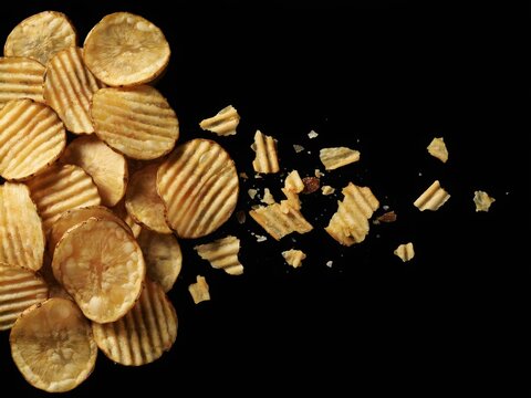 Golden potato chips scattered on black background for snack advertising