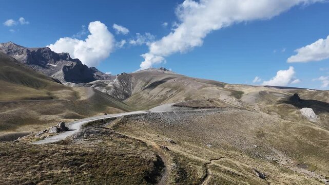 Cinematic shot of a winding dirt road cutting through a remote mountain landscape under a blue sky.