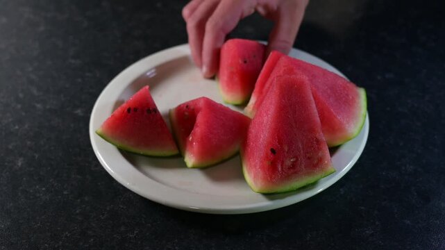 Red delicious watermelon cut into slices on white plate, watermelon video, children and adults take watermelon slices, eat and put the watermelon rind on a plate, healthy food