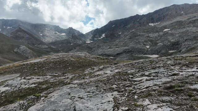Cinematic view of a rugged rocky mountain landscape with dramatic clouds and snow patches.