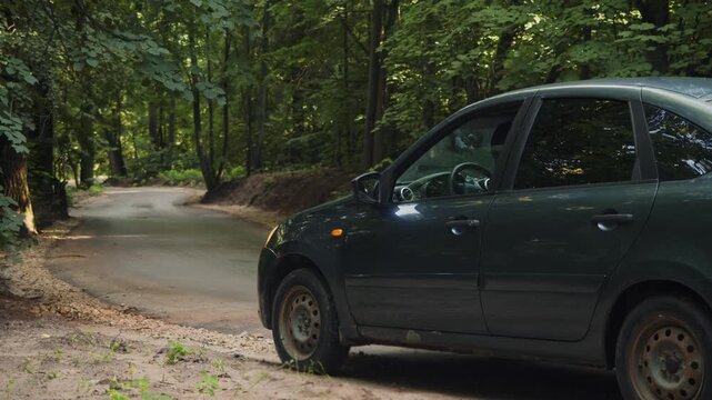 Masked car thief pulls over stolen vehicle on roadside after escape attempt. Wounded criminal gets out holding abdomen and disappears into forest.