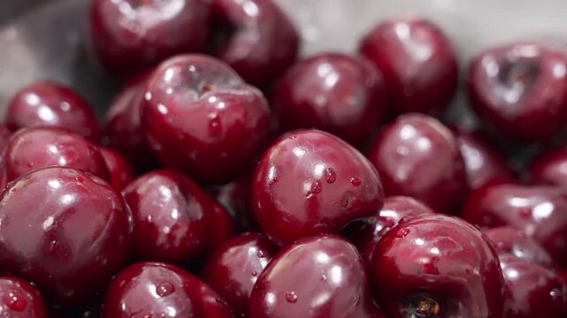 Close-up abstract view of a pile of vibrant, glossy dark red cherries covered in fresh water droplets, perfect for healthy food concepts, summer dessert themes, and natural fruit textures.