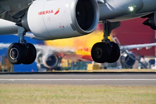MADRID, SPAIN - MAY 29, 2026: Engine nacelle and main gear of an Iberia Airbus A350 900 above the runway at Barajas airport, the colors of a DHL freighter smeared by panning behind it