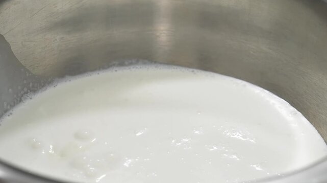 Close-up shot of white granulated sugar being poured into a steaming milk mixture inside a metal pot, preparing a creamy base sauce for a homemade fruit dessert.