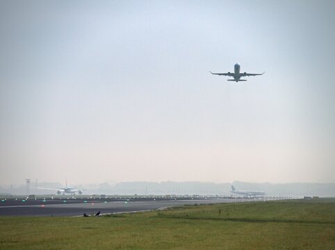 Amsterdam, Netherlands - July 10, 2024: a jet climbs away from the runway at Amsterdam Airport Schiphol in morning haze while another airliner touches down and a third waits on the far side