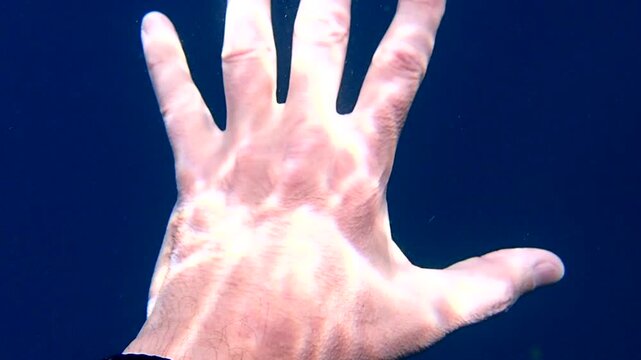 Human hand underwater with abstract light patterns rippling on skin