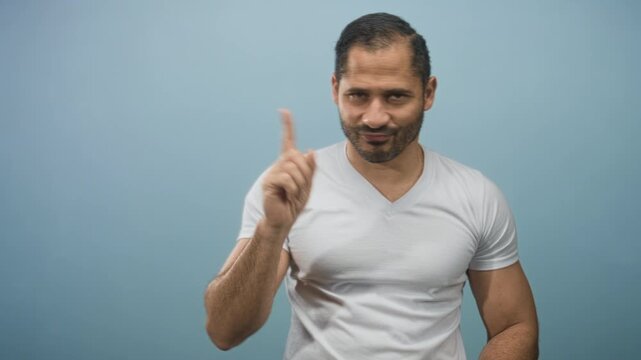 Man in white t shirt points finger forward with stern expression and slight smirk in studio; confidence guidance.