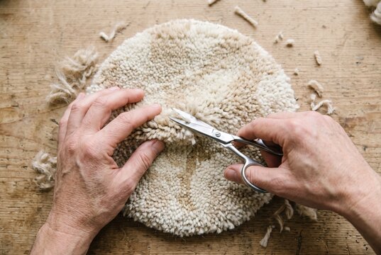 Hands carefully trimming the edges of a round tufted yarn piece with small scissors