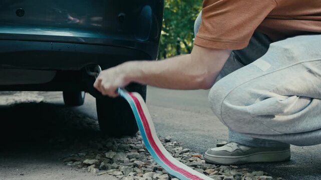 Person attaching tow strap to damaged car after road accident. Vehicle is being pulled from roadside ditch while traffic passes in background.