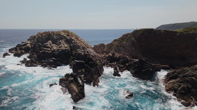 4K static drone footage of Punta Cometa in Oaxaca, Mexico, viewed from low altitude over the sea, with waves breaking against rocky cliffs and a blue ocean horizon in daylight.