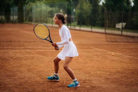 Young girl holding racquet on outdoor clay court during tennis lesson, focus and active youth sport training.