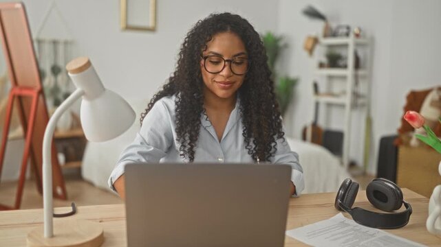 Woman smiling and typing on laptop at a desk in a studio apartment; remote work productivity focused.