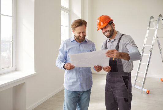 Foreman builder showing renovation plan to man client, posing in empty room with white walls and ladder in background, discussing construction details, renovation strategies for project