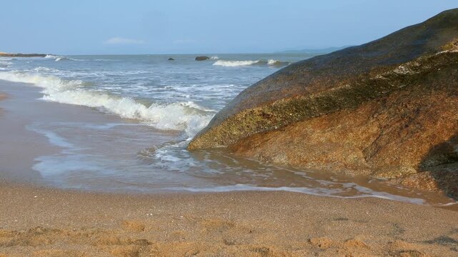 Sea waves washing over large boulders along coastal beach with distant mountains video with sound