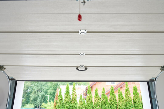 Sectional garage door is partially open with a view outside from inside the garage