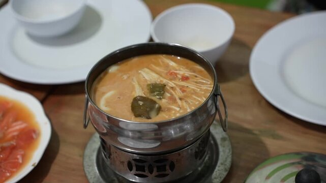 A close-up video shot of a spicy, thick Asian soup with enoki mushrooms, served piping hot in a metal pot on a restaurant table, showcasing the rich broth and an authentic dining atmosphere.