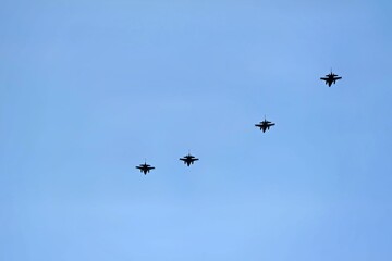 Fototapeta premium A formation of four fighter jets flying across a clear blue sky. The sleek aircraft are seen in a straight line, showcasing their design and military capability.
