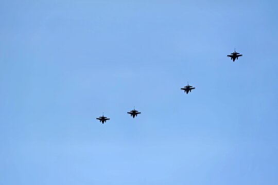 A formation of four fighter jets flying across a clear blue sky. The sleek aircraft are seen in a straight line, showcasing their design and military capability.